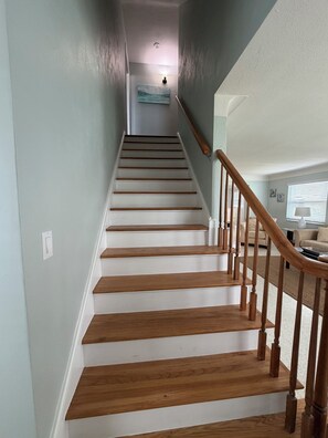 Eine Treppe mit Holzboden und einem Holzgeländer, die zu einem Raum mit hellblauer Wand und einem Gemälde führt.
