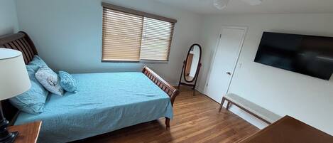 Un dormitorio con cama, cómoda, tocador, ventilador de techo, ventana con persianas y televisión montada en la pared.