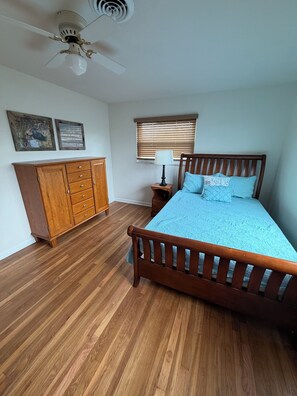 Ein Schlafzimmer mit einem Holzbett, einem Nachttisch, einer Kommode, einem Deckenventilator und einem Fenster mit Jalousien.