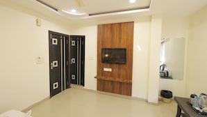 A room with a bed, a TV mounted on a wooden panel, a mirror, and a bench with bottles. - V One Hotel Shiv Shakti (Ujjain)