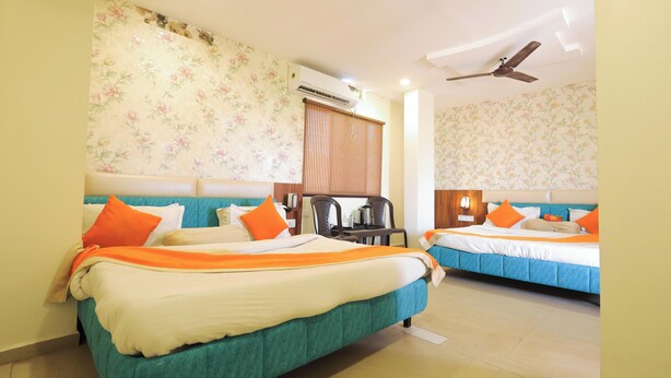 A hotel room with two beds, a ceiling fan, an air conditioning unit, and a window with blinds. - V One Hotel Shiv Shakti (Ujjain)