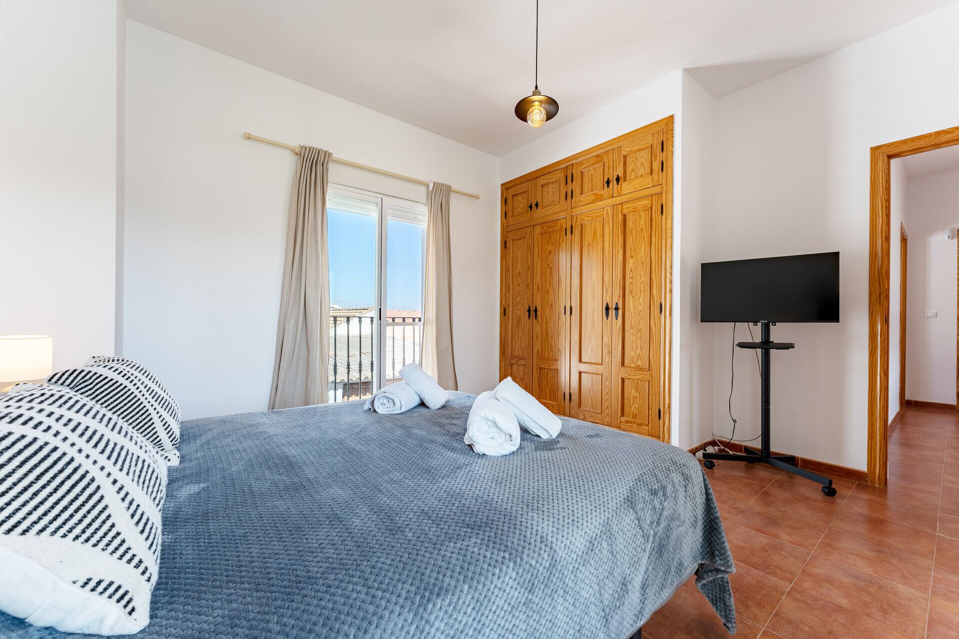 Ein Schlafzimmer mit Bett, Kleiderschrank, Fernseher auf einem Schrank und einem Fenster mit Vorhängen.
