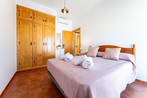 Un dormitorio con un amplio armario de madera, una cama con cabecero y una mesita de noche.