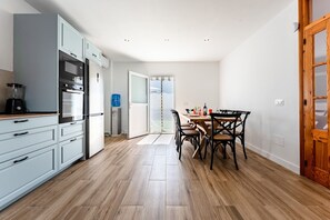 A modern kitchen with a dining area, wooden flooring, and a view through a glass door. - MalagaSuite Villa Flor de Piedra (Fuente de Piedra)
