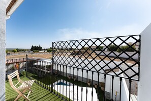 Un balcón con vista a una piscina, una silla de madera y un cerramiento de celosía.