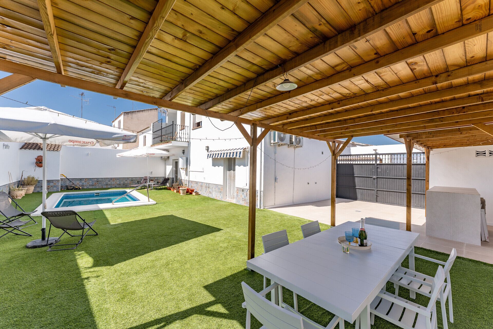 Un espace extérieur abrité comprenant une piscine, une table avec des chaises et une pelouse.