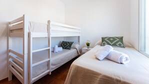 Et værelse med to køjesenge, en enkelt seng, et lille natbord med en lampe og et vindue med naturligt lys.