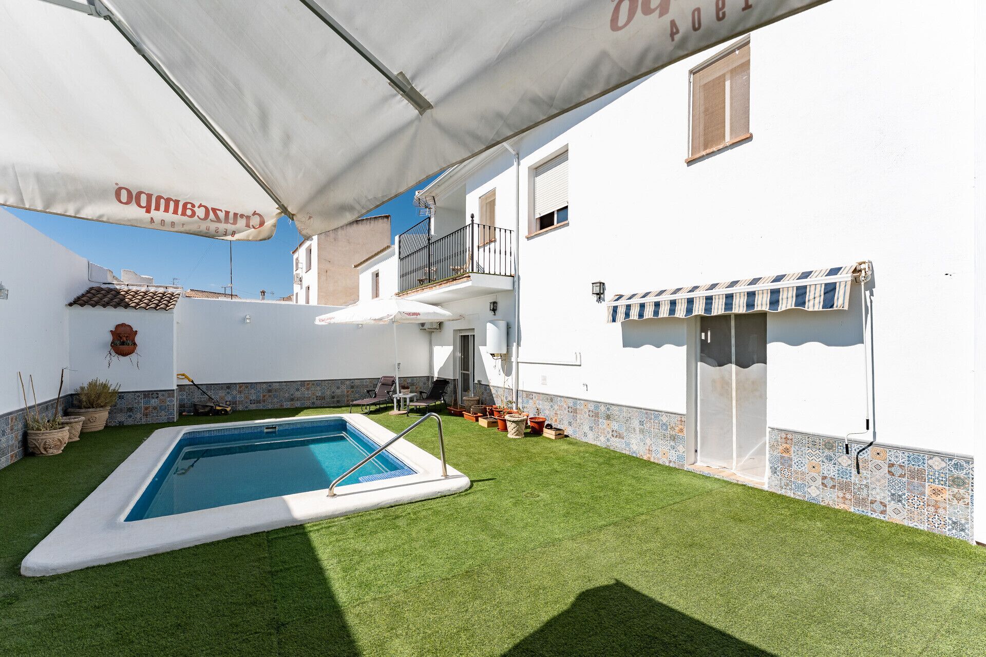 Ein Schwimmbad mit weißer Liegefläche, umgeben von einer gepflegten Rasenfläche, und ein Gebäude mit einer Kachelfassade und einem Balkon.