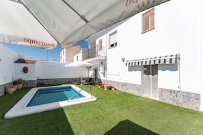 A swimming pool with a white deck, surrounded by a well-maintained lawn, and a building with a tiled facade and a balcony. - MalagaSuite Villa Flor de Piedra (Fuente de Piedra)