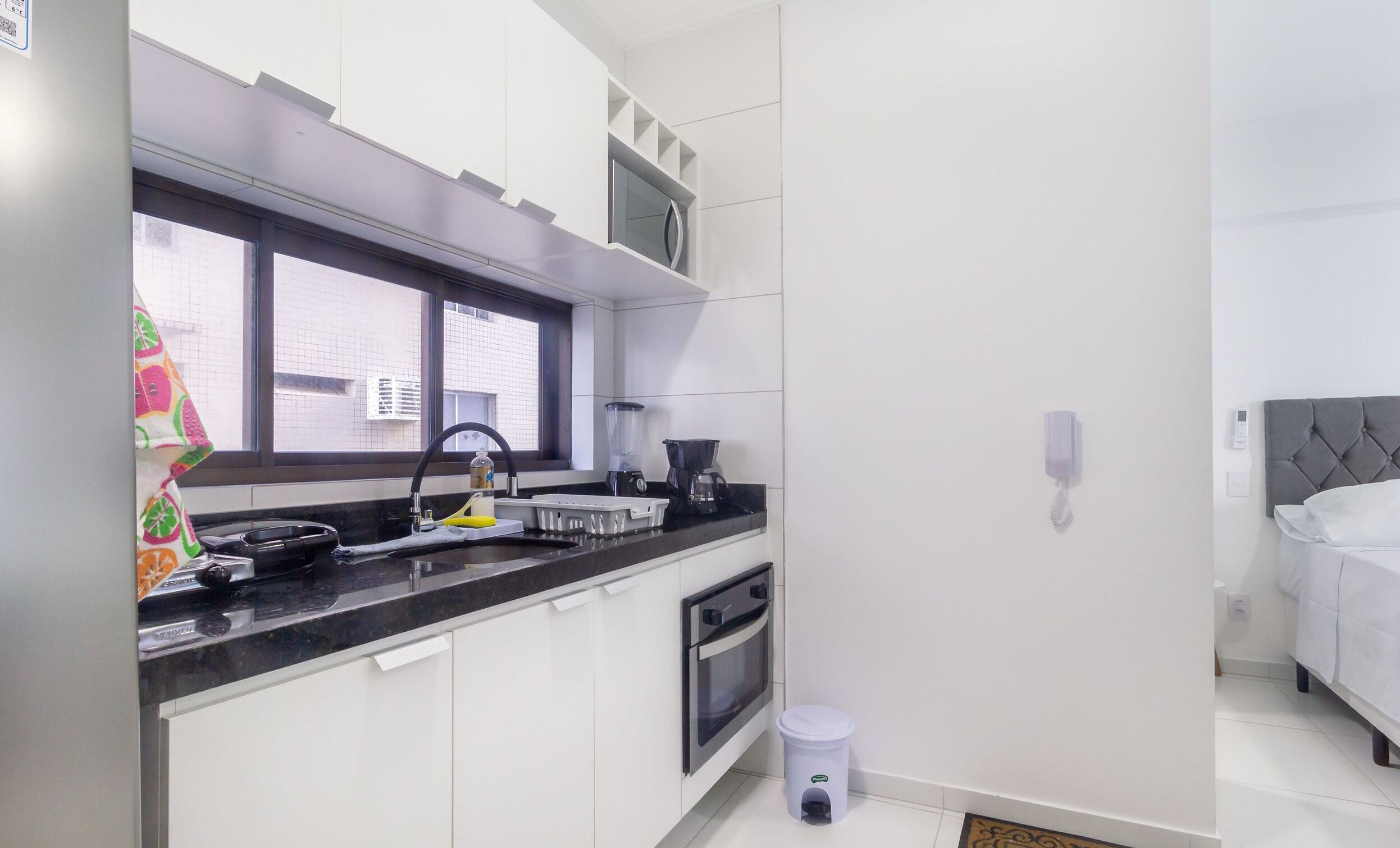 A modern kitchen with a black countertop, white cabinets, a window, and a small trash bin.