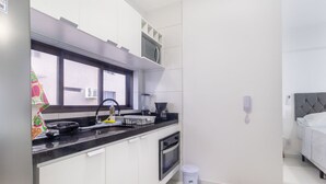 A modern kitchen with a black countertop, white cabinets, a window, and a small trash bin. - Studio w/ sea View in Bldg w/ gym - Iaa0504 (Recife)