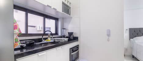 Una cocina moderna con encimera negra, armarios blancos, una ventana y un pequeño cubo de basura.