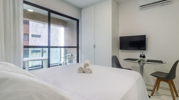 A hotel room with a bed, a TV, a small table with chairs, and a window with a view of buildings. - Studio w/ sea View in Bldg w/ gym - Iaa0504 (Recife)
