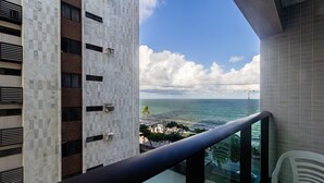 A balcony with a view of the sea and a building with a checkered facade. - Studio w/ sea View in Bldg w/ gym - Iaa0504 (Recife)