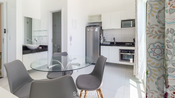 Une cuisine moderne avec des meubles blancs, un réfrigérateur en acier inoxydable et un four à micro-ondes. On y trouve une table à manger en verre, accompagnée de deux chaises.