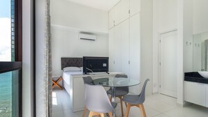Une chambre d’hôtel moderne équipée d’un lit, d’un bureau avec un ordinateur, de deux chaises, d’une table en verre et offrant une vue sur la mer.