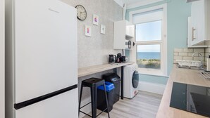 Eine kompakte Küche mit Waschmaschine, Kaffeemaschine und Meerblick durch ein Fenster.