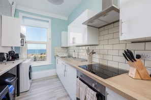 Uma cozinha moderna com vista para o mar, com armários brancos, fogão preto e bancada de madeira.
