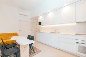 Una cocina moderna con armarios blancos, microondas integrado y horno de acero inoxidable.