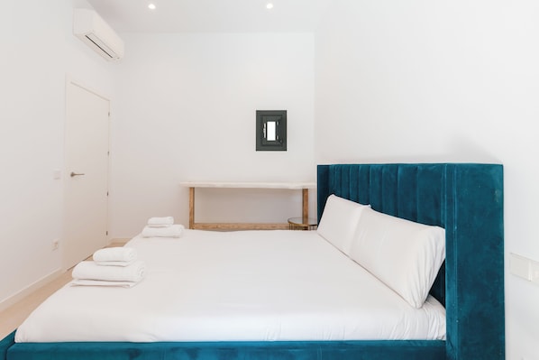 A hotel room with a bed, a bedside table, a wall-mounted air conditioner, and a door.