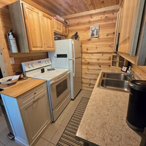 Une cuisine de taille réduite, dotée de meubles de rangement en bois, d’une cuisinière blanche, d’un réfrigérateur et d’un évier.