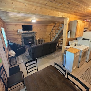 L’intérieur chaleureux d’un chalet comprend un espace de vie, une cheminée, une table à manger et une cuisine équipée d’une cuisinière et d’un réfrigérateur.