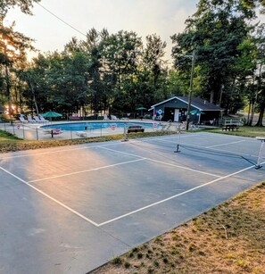 Un court de tennis avec un filet, entouré d’arbres et bordé d’un petit bâtiment.