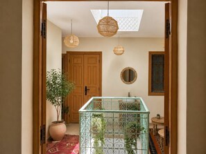 Una habitación con puerta de madera, planta en maceta, baranda de vidrio y lámpara colgante.