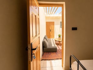 Una habitación con una cama, un sofá, una mesita con una planta y una puerta que da a otra habitación.