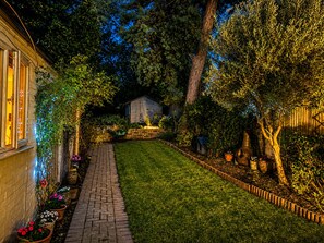 A well-maintained garden with a paved pathway, a wooden shed, and various potted plants.