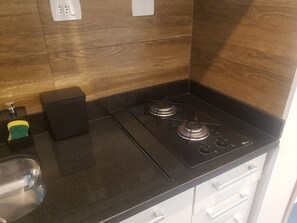 A kitchen with a black countertop, two gas burners, a black stove, a trash bin, and a soap dispenser. - 215 Studio in Campinas/SP City Center (Campinas)