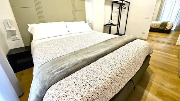 Hotellihuone, jossa on suuri sänky, yöpöytä, peili ja vaatekaappi.