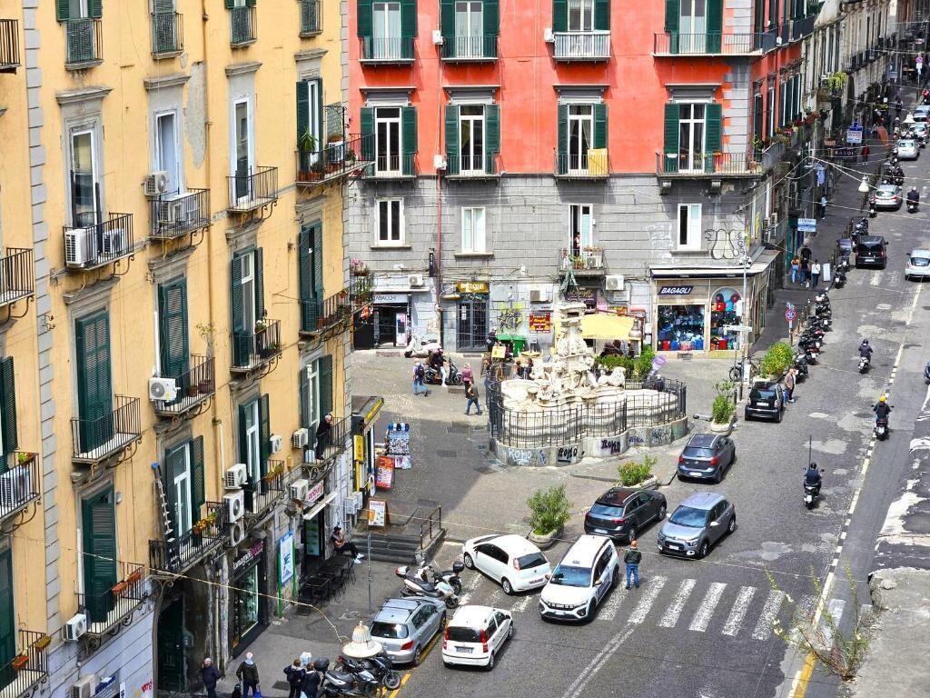 A street view with buildings, a fountain, and parked cars.