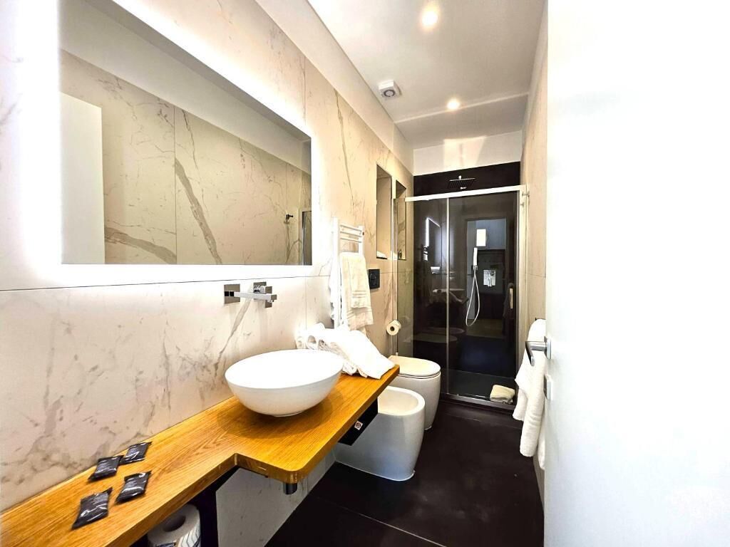 A modern bathroom with a large mirror, a wooden vanity, a white sink, a toilet, and a glass shower enclosure.