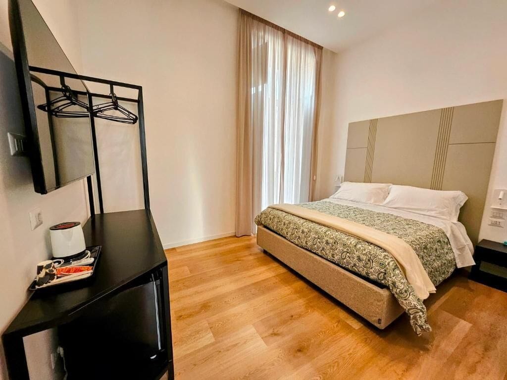 Habitación de hotel con cama, mesita de noche, espejo y ventana con cortinas.