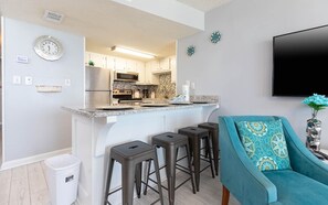 Une cuisine moderne dotée d’un îlot central, de tabourets de bar, d’un évier et d’un coin repas avec un canapé de couleur turquoise.