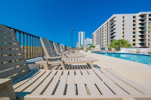 A poolside area with sun loungers and a swimming pool, surrounded by high-rise buildings. - Island Winds East 508 2 Bedroom Condo (Gulf Shores)