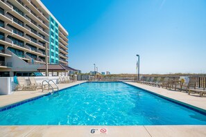 Une piscine dont la profondeur est indiquée à 6 pieds, des chaises longues et un bâtiment doté de balcons.