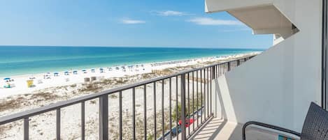 A balcony with a view of a beach, a railing, and a chair.