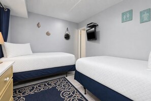 A hotel room with two beds, a desk, a lamp, a TV, and decorative shells on the wall. - Island Winds East 508 2 Bedroom Condo (Gulf Shores)