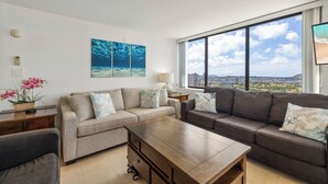 A modern living room with a sofa set, a coffee table, and a view of a cityscape through large windows. - Stunning Panoramic Ocean Views! 2bd/2Ba PH (Honolulu)