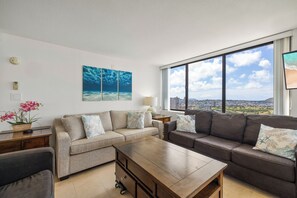 Ein modernes Wohnzimmer mit einer Sofagarnitur, einem Couchtisch und Blick auf eine Stadtlandschaft durch große Fenster.