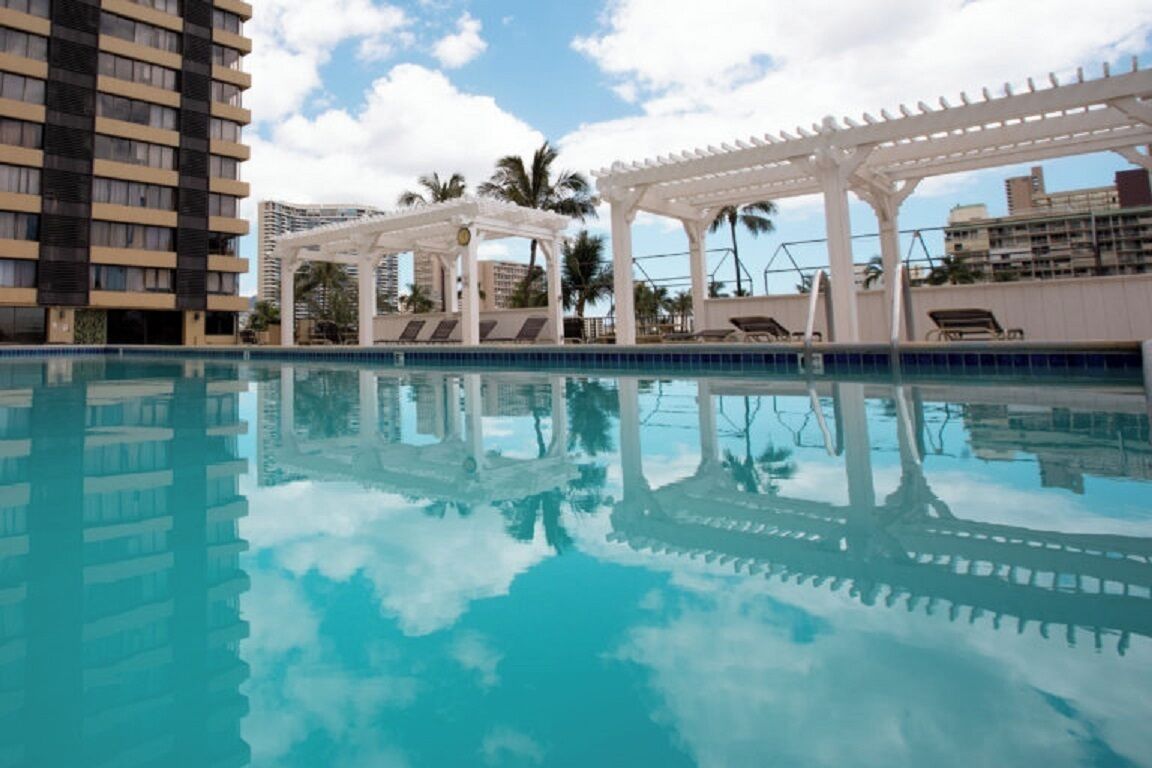 A swimming pool with a clear reflection, surrounded by white pergolas and lounge chairs.