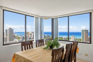Ein Essbereich mit einem großen Tisch und Stühlen, große Fenster mit Blick auf Stadt und Meer.