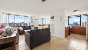A spacious living area with a large window, a ceiling fan, and a kitchen with a view. - Stunning Panoramic Ocean Views! 2bd/2Ba PH (Honolulu)