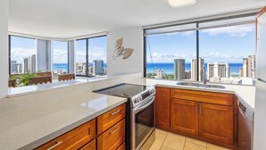 A modern kitchen with a large window, a view of the city, and a dining area with a table and chairs. - Stunning Panoramic Ocean Views! 2bd/2Ba PH (Honolulu)