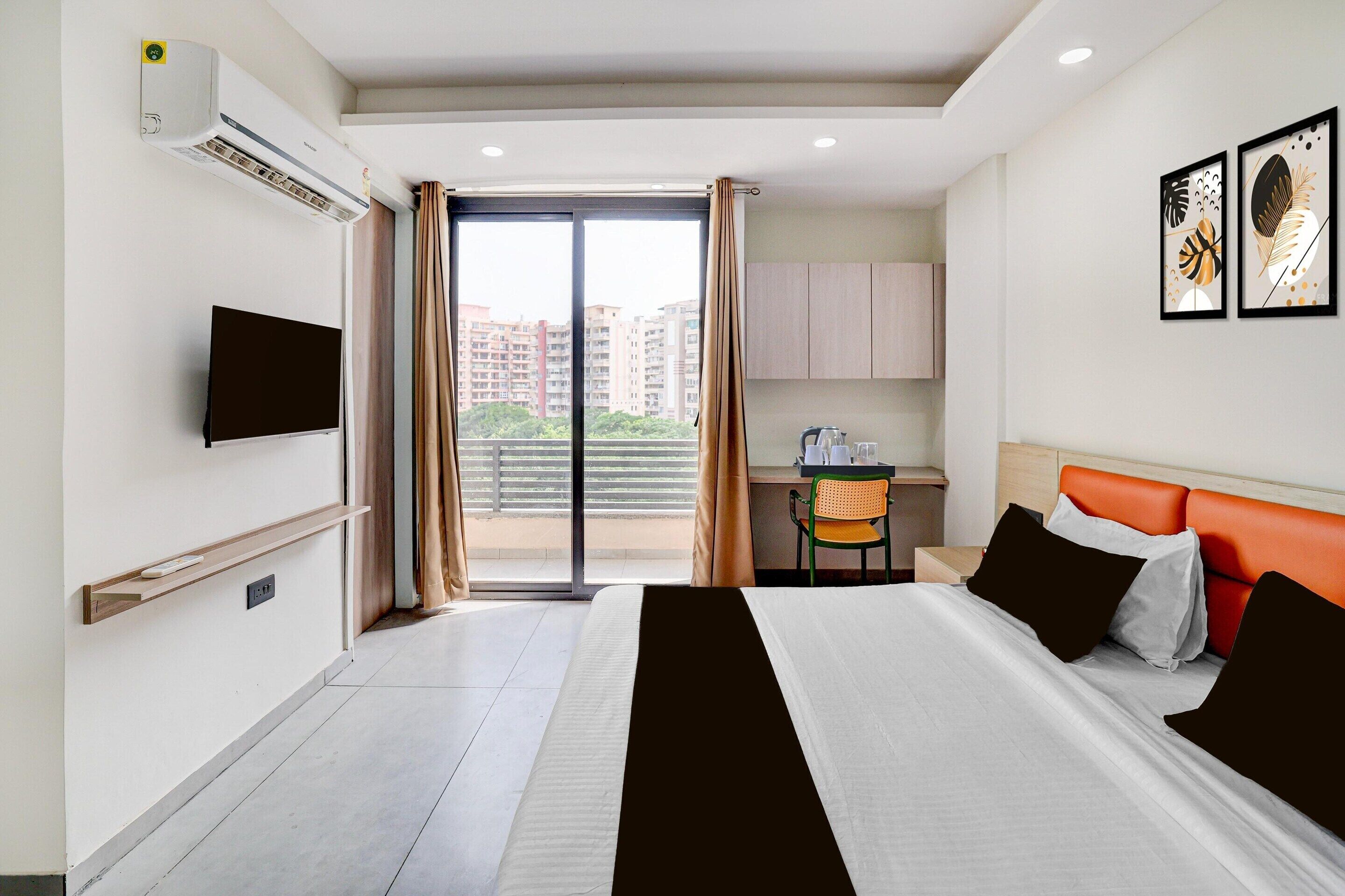 Une chambre d’hôtel avec un lit, un bureau, une chaise, une télévision et une vue sur les immeubles par la fenêtre.