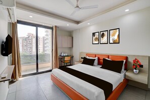 A hotel room with a bed, a desk, a chair, a TV, and a window with a view of buildings. - Classic With Balcony Townhouse Sector 52 (Gurugram)