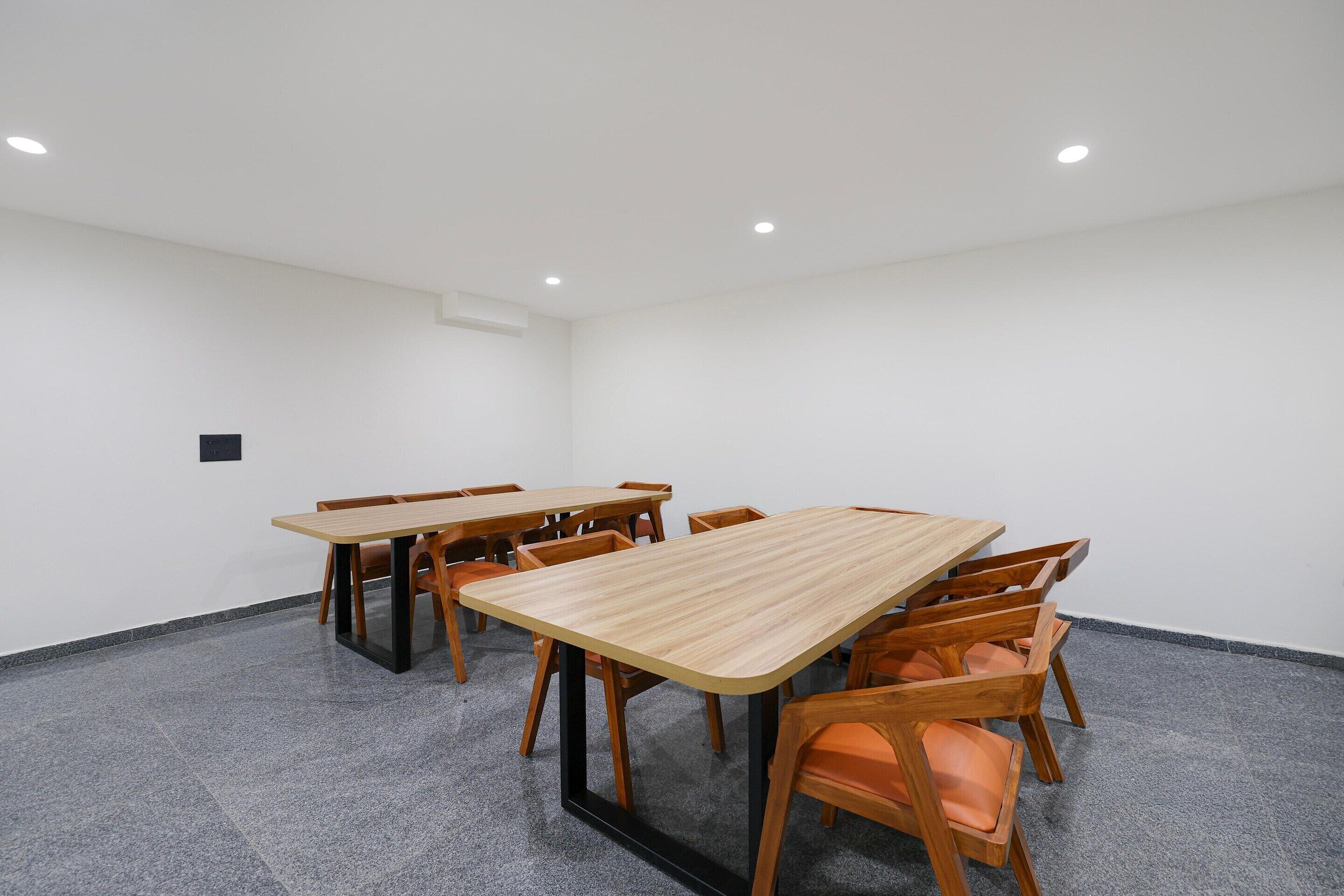 A conference room with a large rectangular table surrounded by chairs, white walls, and a carpeted floor.