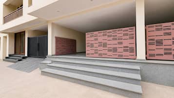 L’entrée d’un immeuble est marquée par un escalier menant à une zone abritée, une porte noire et un mur aux motifs rouges et roses.